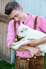 blond bavarian man holding a little white goat