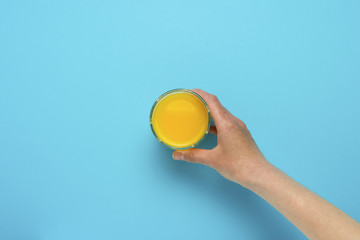 Female hand taking orange juice on a blue background. Flat Lay Still Life Table Top View Blue...