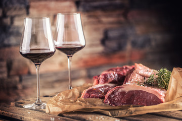 Two cups with red wine and raw beef steak on wooden table