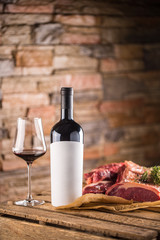 Naklejka premium Cup and a bottle of red wine and raw beef steak on wooden table