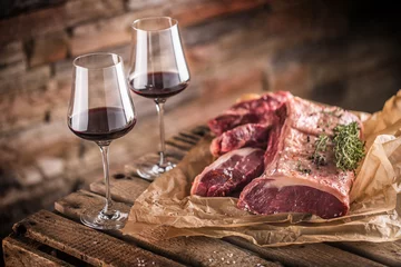 Tuinposter Two cups with red wine and raw beef steak on wooden table © weyo