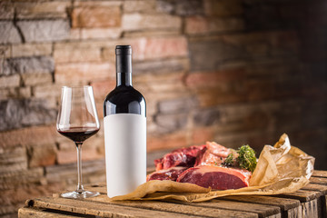 Cup and a bottle of red wine and raw beef steak on wooden table