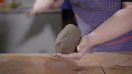 female hands are kneading and beating clay in art pottery workshop, shaping ball for making ceramic goods