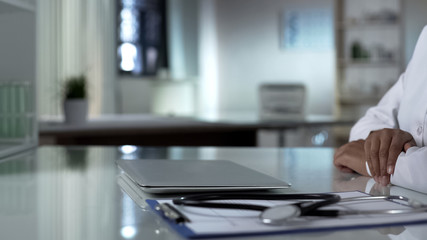 Doctor sitting at table with closed laptop, starting new workday in clinic