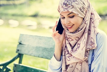 Islamic woman using mobile phone with smiling at park