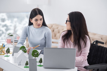 Modern village. Young immobile woman and colleague sitting at table while using laptop