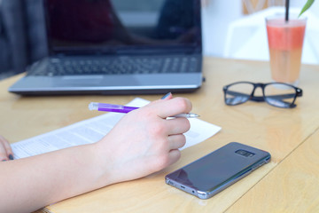 Close-up of a female hand. Study the contract, make notes on new projects. Desktop - laptop, smartphone, glasses, notebook.