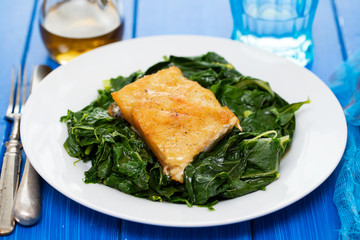 fried cod fish with greens on white plate on blue background