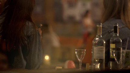 Wine and glasses on bar counter, two women drinking alcohol at club, back view