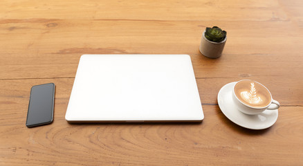 Modern laptop with cup of coffee and mobile phone on wooden table