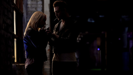 Man lighting cigarette for woman, smoking at night club, young couple flirting