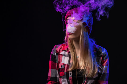 Vaping girl. Young hipster woman vape e-cig on studio on black background. Hip-hop style. Close up.