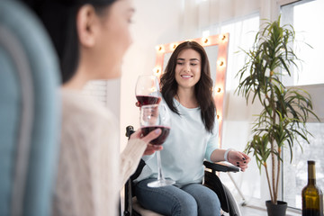 Lets celebrate. Charming handicapped woman drinking wine and talking to friend