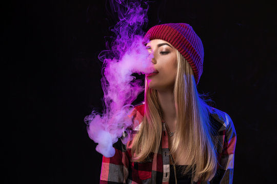 Vaping girl. Young hipster woman vape e-cig on studio on black background. Hip-hop style. Close up.