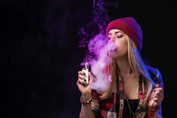 Vaping girl. Young hipster woman vape e-cig on studio on black background. Hip-hop style. Close up.