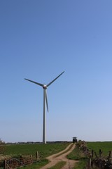 Wind turbine with tracor coming down mud road in field