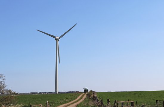 Wind turbine with tracor coming down mud road in field