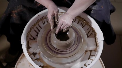 skilled craftsman is shaping and correcting clay cup on a wheel-head sitting in a pottery creative workshop, top view