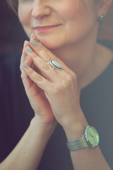 Smiling woman wearing silver wristwatch and blue dress holding hands close to chin
