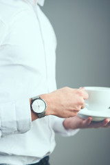 Young man wearing silver wristwatch and white plain shirt holding cup of coffee
