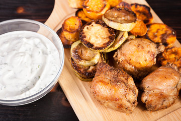 Dinner made of fried chicken and grilled vegetables and a glass bowl of sour cream souce