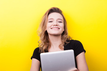 Naklejka premium Beautiful student woman holds a laptop in hands on yellow background in studio photo