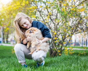 Cute teen girl with blond hair playing with her Pomeranian puppy on green grass in the park