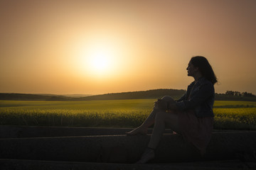 Silhouette of a girl and sunset over canola fields