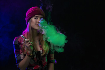 Fototapeta premium Vaping girl. Young hipster woman vape e-cig on black background. Hip-hop style. Studio shot
