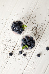 top view of arranged chia puddings with fresh blueberries and mint on white wooden surface