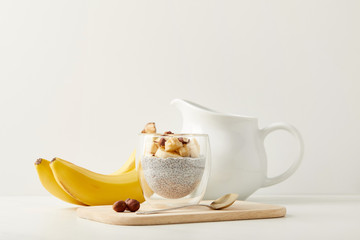 close up view of tasty chia seed pudding with bananas and hazelnuts on white tabletop