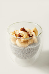 close up view of tasty chia seed pudding with pieces of banana and hazelnuts on white tabletop