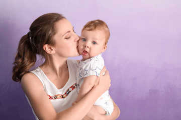 Young mother with her cute little baby on color background