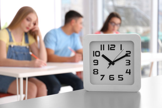 Clock and blurred students passing exam on background