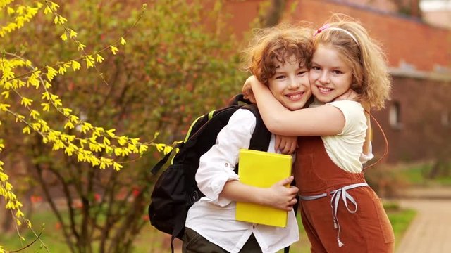 Schoolchildren, brother and sister, boy and girl hug against the background of a blossoming spring tree. Day of knowledge. Back to school. School friendship