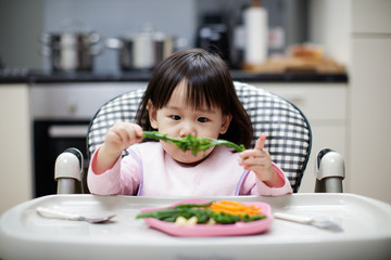 Baby girl eating healthy vegetable at home
