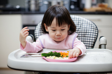 Baby girl eating healthy vegetable at home