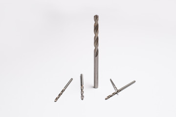 A few drills for a drill. A large drill stands, and four little ones lie side by side. Drills isolated on white background. Side view from above. Close-up photo