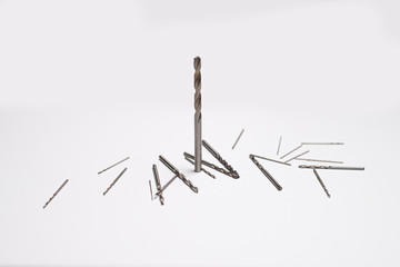 A few drills for a drill. A large drill stands, and the little ones lie side by side. Drills isolated on white background. Side view from above. Close-up photo