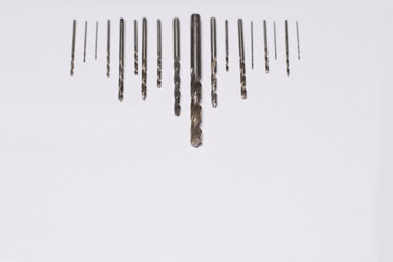 Large and small drills for drilling lie in a row on a white isolated background. Shallow depth of field. Focus on the tip of a large drill. View from above.