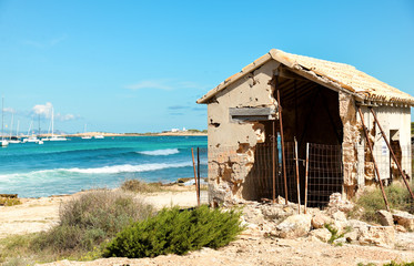 Ibiza, Spain - October 5, 2017 : View of lonely old house on beach near blue water, on Ibiza and Formentera island. Summer holidays and free time at sunny weather near sea.