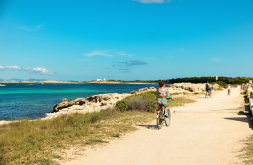 Fototapeta na wymiar Ibiza, Spain - October 5, 2017 : View of road with car and bicyclist riding on pear. Big green palm tree on Ibiza and Formentera island beach. Summer holidays and free time at sunny weather near sea.