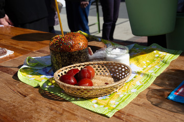 wicker basket stands with an easter cake and a burning candle on the street in the morning near the...