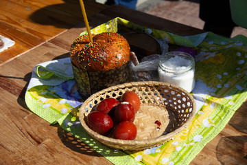 wicker basket stands with an easter cake and a burning candle on the street in the morning near the...