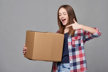 Delivery, relocation and unpacking. Happy excited young woman holding cardboard box pointing emotionally at box