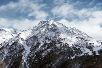 Alpine mountain landscape. High mountain covered with snow on a background cloudy sky