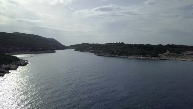 Aerial: Flying over beautiful bay on island Vis in Croatia at evening. Sun reflecting from blue sea water. Filmed on sailing trip in Adriatic sea in Croatia.