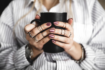 Female hands holding a white cup of tea, burgundy manicure