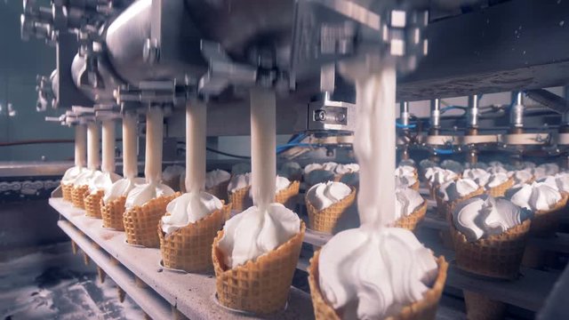 Lines of waffle cones are getting filled with ice-cream substance