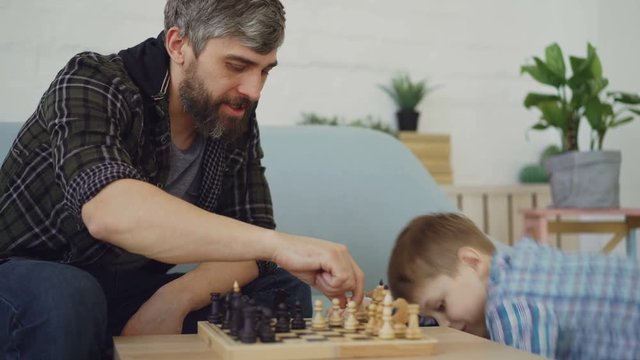 Loving dad is playing chess with his little child, teaching him rules and talking to him. Raising children, intellectual games and happy childhood concept.
